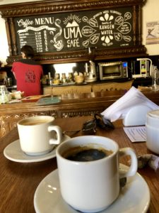 Coffee cups in foreground, barista making coffee in background in front of menu