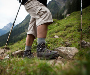 Man hiking with hiking poles, wearing boots with mountain in background